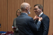 The rector is pinning a decoration onto a man during the ceremony.