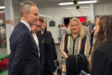 Four people are standing together in the hall and having a conversation. A man in a suit is addressing three women standing opposite him.