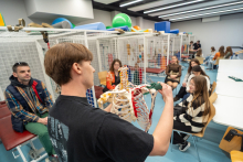 A person leading a class shows a model of the upper‑limb skeleton, explaining the structure and joint mobility to a group of participants seated in a therapy room.