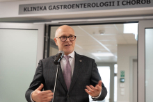 A person in a suit speaking into a microphone during an event, standing in front of the entrance to the Gastroenterology and Internal Medicine Clinic.