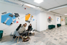 A section of the university corridor with colorful graphics on the wall illustrating various stages of the faculty’s development, marked with the dates 2001, 2004, and 2026–. Next to them are green sofas and single chairs.