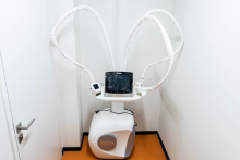 An Icoone treatment device with flexible arms and a touchscreen, placed in a small, bright room.