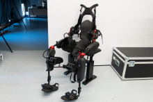 An advanced rehabilitation exoskeleton with a seat, numerous supports, and adjustable fastening elements, positioned in a bright room next to a large transport crate