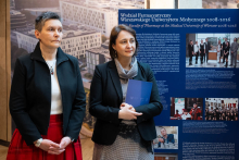 Two people standing in front of an exhibition panel presenting the history of the Faculty of Pharmacy of the Medical University of Warsaw from 2008 to 2026; one of them is holding a navy-blue folder