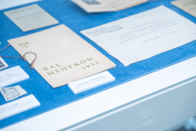 A display case featuring historical documents, including the Bal Medyków 1932 program and other printed materials arranged on a blue surface.