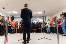 A person speaking into a microphone during an official event, with several other attendees standing behind.