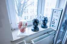 Anatomical head models and training devices placed on a windowsill next to a control panel in a bright room.