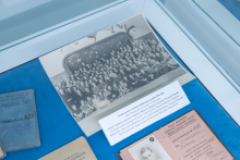 A display case containing a large black‑and‑white group photograph along with old identification documents and cards arranged on a blue surface