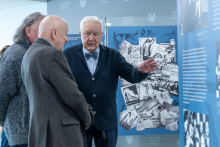 Several people standing in front of an exhibition panel, viewing and discussing a collage of historical posters and printed materials.