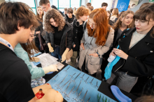 A group of participants gathered at a booth presenting a set of medical tools and training models, observing a demonstration conducted by a person on the other side of the table.