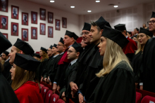 Several dozen people in black academic gowns stand and take the doctoral oath.