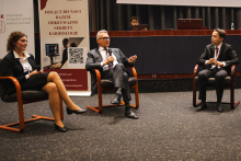 Trzech prelegentów siedzących na scenie w fotelach podczas panelu dyskusyjnego na wydarzeniu kardiologicznym; każda z osób trzyma mikrofon. W tle widoczne są roll‑upy organizatora oraz elementy sali konferencyjnej.