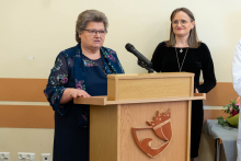 Kobieta stojąca przy mównicy wygłasza przemówienie podczas uroczystości, obok niej stoi druga osoba.