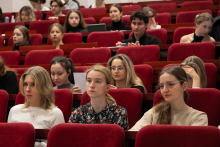 Grupa osób siedząca w czerwonych fotelach w audytorium. 