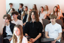 Uczniowie siedzą w sali i uczestniczą w wykładzie, skupiając uwagę na prelegencie lub prezentacji.