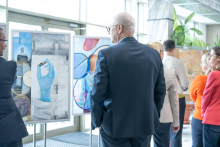 Attendees view framed artworks displayed on easels in a well-lit indoor space, with people standing close to the exhibits.