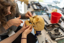 Hands use a medical instrument inside a skull model secured in a clamp, with surgical tools laid out on the table.