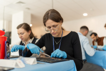 Participants wearing protective gloves perform detailed manual work on small specimens or training materials arranged on blue medical drapes at individual workstations.