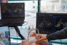 Stanowisko do nauki ultrasonografii: głowica USG przykładana do fantomu treningowego, a obok dwa monitory wyświetlające obrazy przekrojów ultrasonograficznych w czasie rzeczywistym.