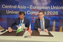 Two representatives seated at a signing table, handling official documents, with pens on document folders and two small national flags placed between them.