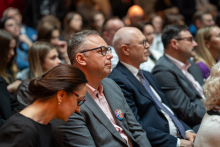 A close-up of the audience seated in the hall during the event. Rows of people in elegant attire can be seen, focused on what is happening in front of them.