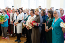 A group of medical professionals are standing together during a ceremony; several individuals are holding flowers and wrapped gifts.