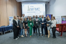Grupa elegancko ubranych osób pozuje do wspólnego zdjęcia. W tle widać ekran multimedialny ze slajdem z logo WIMC.