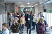 Duża grupa osób przechadza się korytarzem budynku. Część osób idzie w stronę aparatu, inne osoby rozmawiają lub rozglądają się dookoła.