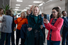  Dwie osoby stoją w holu. Jedna z osób trzyma w dłoni telefon i wykonuje zdjęcie lub nagranie, a druga osoba stoi obok z rękami skrzyżowanymi.