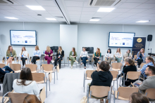 Kobiety siedzą w półokręgu w sali konferencyjnej i prowadzą panel dyskusyjny. Część kobiet trzyma w rękach mikrofony, pozostałe mają dłonie oparte na kolanach. Naprzeciwko siedzi publiczność, zwrócona w stronę panelistek.