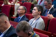 Kilka osób siedzi w pierwszym rzędzie sali wykładowej. Wszystkie patrzą w stronę sceny i słuchają wystąpienia. 