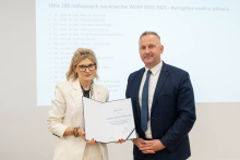 A woman and a man are posing for a photo. The woman is holding an open diploma in her hands.