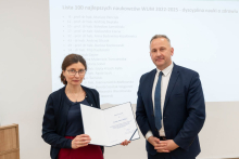 A woman and a man are posing for a photo. The woman is holding an open diploma in her hands.