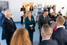 Several people stand and talk in a room. One person is holding a document with a red edge.