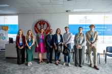 A group of people stands in a conference room; some individuals are holding bags, with screens displaying “Student Scientific Conference” in the background.