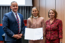 A man and two women are posing together for a photo. The woman in the middle is holding an open diploma in her hands.