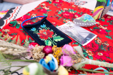 Embroidered items, cards, and dried flowers lie on a patterned red fabric. In the center, there is a small pouch with a floral motif.