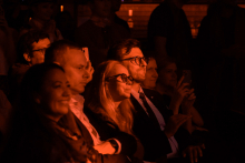 Three people are sitting in the darkness in the audience.