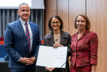 A man and two women are posing together for a photo. The woman in the middle is holding an open diploma in her hands.