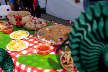 A table covered with a checkered tablecloth displays various dishes. Pasta, dumplings, and pieces of fruit are visible. Small Philippine flags are placed on the dishes.
