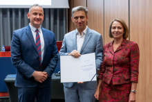 Two men and a woman are posing together for a photo. The man in the middle is holding an open diploma in his hands.