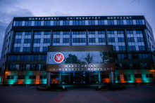 The building of the Medical University of Warsaw seen from the outside after dark. The name of the university is visible on the facade, along with the illuminated main entrance.