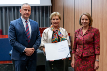 A man and two women are posing together for a photo. The woman in the middle is holding an open diploma in her hands.
