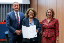 A man and two women are posing together for a photo. The woman in the middle is holding an open diploma in her hands.