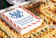A cake with the inscription “Medical University of Warsaw” is placed on a large tray. Various sweets are arranged around it.
