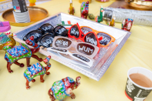 Colorful animal figurines and glasses with the words “WUM” and “INDIA” lie on a metal tray. A cup with a drink stands nearby.