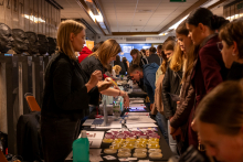 An educational stand in a museum corridor. At a long table, presenters talk with visitors, and brochures, equipment, and colorful samples for demonstrations are arranged on the surface.