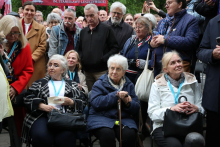 Grupa siedzących uczestników wydarzenia, część osób trzyma torebki lub laskę. Za nimi stoją kolejne osoby zgromadzone na uroczystości. W tle widoczny jest baner z odniesieniem do Stanisławy Leszczyńskiej.