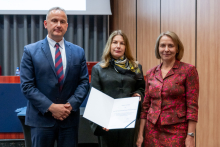 A man and two women are posing together for a photo. The woman in the middle is holding an open diploma in her hands.