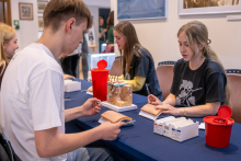 Practical activities at a table – participants work with anatomical skin models and educational tools. Medical containers and training materials are visible on the table.